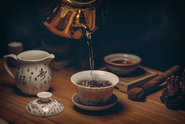 Chinese tea cups with kettle pouring water over tea leaves