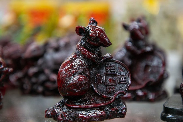 Brownish red rat figurine holding lucky coin