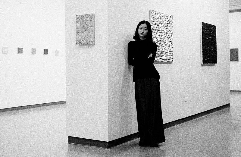 Artist Yingqian Cao in long black dress in art gallery with her work