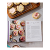 Cookbook open to a page with cookie recipe and cookies on a cooling rack