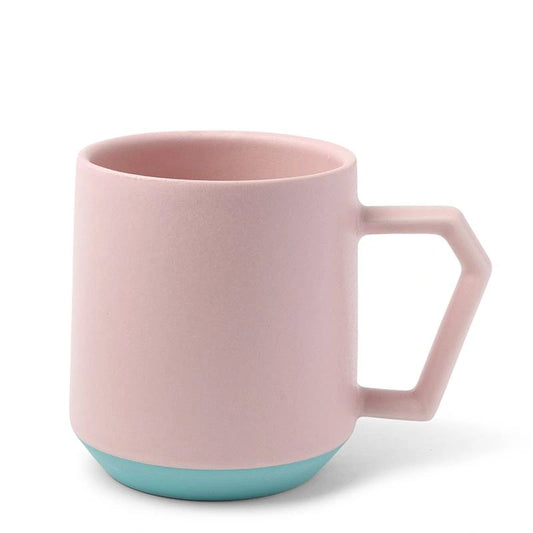 A pastel pink mug with a geometric handle and a light teal base. The design is modern and minimalist, conveying a clean and simple aesthetic.