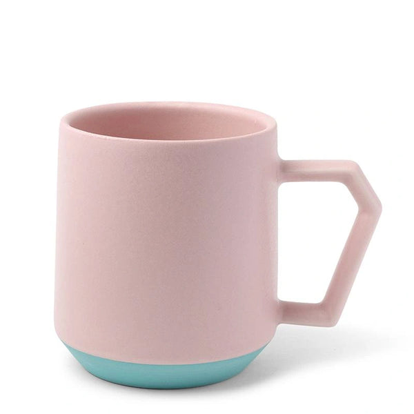A pastel pink mug with a geometric handle and a light teal base. The design is modern and minimalist, conveying a clean and simple aesthetic.