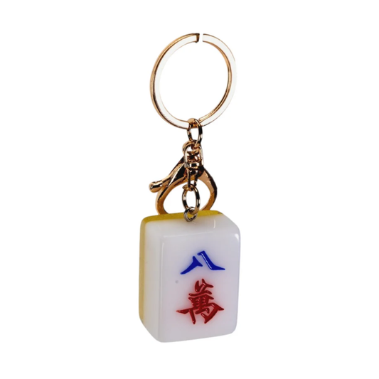 A novelty keychain shaped like a mahjong tile, featuring a white face with red and blue Chinese characters, a gold-tone metal clasp, and a split key ring on a plain white background.
