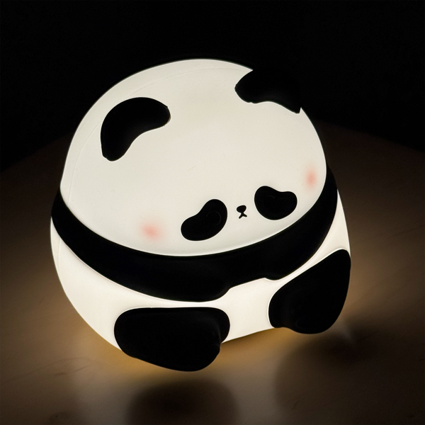A round, glowing panda night light with a black and white design, resting on a dark surface against a black background.