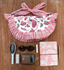 flat lay of pink and white bag on wooden background with various items below (sunglasses, wallet, hairbrush, notebook and pen)
