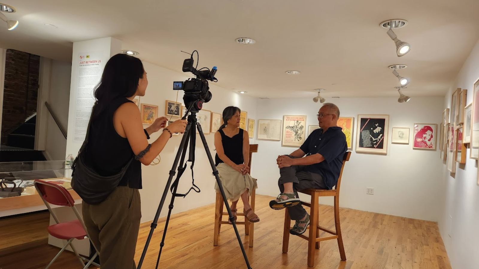 Woman interviewing man in art gallery while woman films with camera