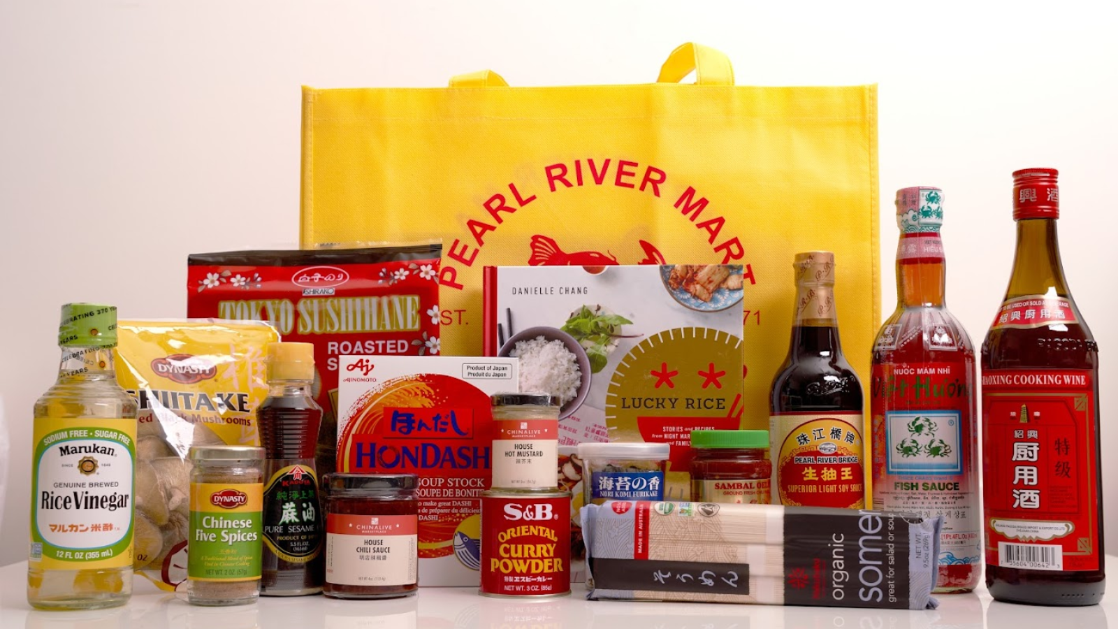 Array of Asian cooking ingredients with cookbook in front of yellow Pearl River Mart bag