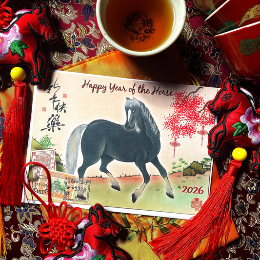 Card with a horse illustration and text 'Happy Year of the Horse' surrounded by decorative items on a patterned fabric background.