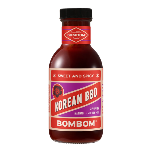 A bottle of Bombom Korean BBQ Sweet and Spicy marinade sauce, featuring a red and purple label with white lettering, set against a plain white background.