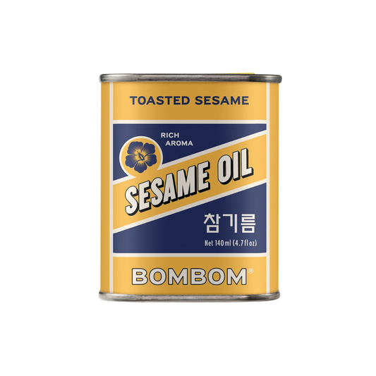A can of Bombom Toasted Sesame Oil on a plain white background. The can features a yellow and navy blue label with the brand name 'BOMBOM' and 'SESAME OIL' in bold white lettering.
