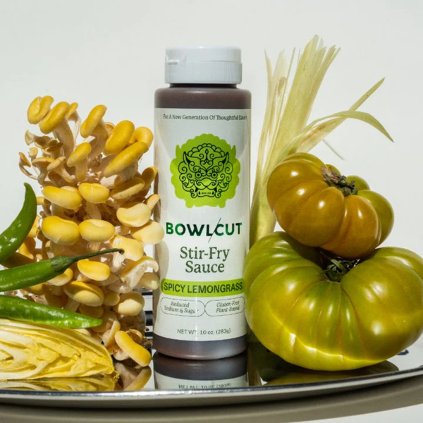 Bottle of Bowlcut Stir-Fry Sauce surrounded by vegetables on a white background