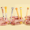 Set of cartoon animal-themed pens held by hands on a yellow background