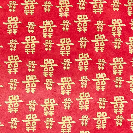 Red paper with a repeating pattern of gold Chinese double happiness symbols.