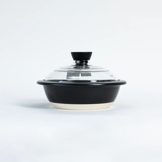 A black ceramic casserole dish with a clear glass lid and black knob, set against a plain white background.