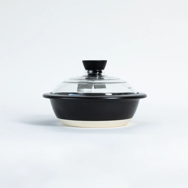 A black ceramic casserole dish with a clear glass lid and black knob, set against a plain white background.
