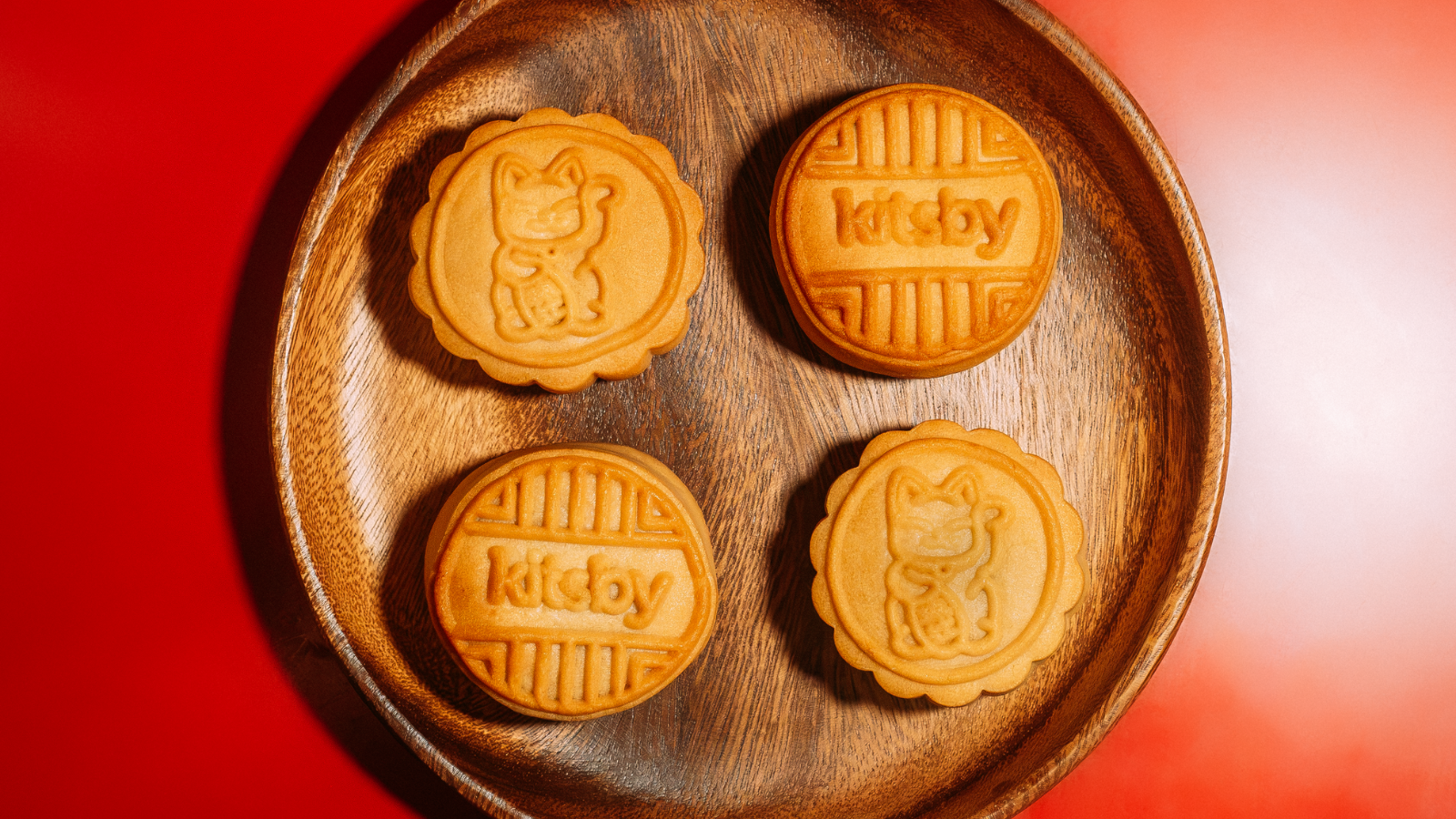 Four mooncakes on a wooden tray against a red background
