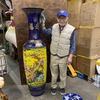 Man holding a large decorative vase in a storage area with boxes and other items.