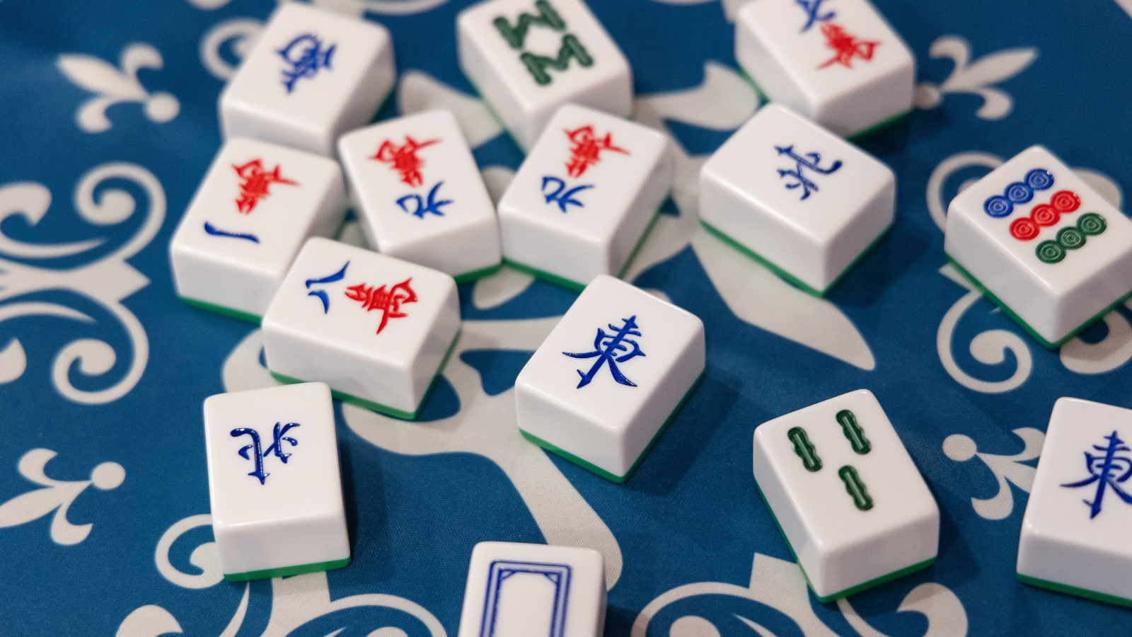 Scattering of various mahjong tiles on blue and white mat