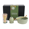 Ceremonial matcha set with green packaging, including a bowl, whisk, and scoop on a white background.