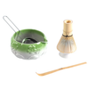 Green ceramic whisk holder with floral designs, bamboo whisk, and wooden scoop on a white background