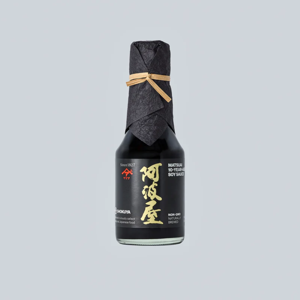 A bottle of soy sauce with a black label and black paper-wrapped neck, tied with a tan string, centered on a light gray background.