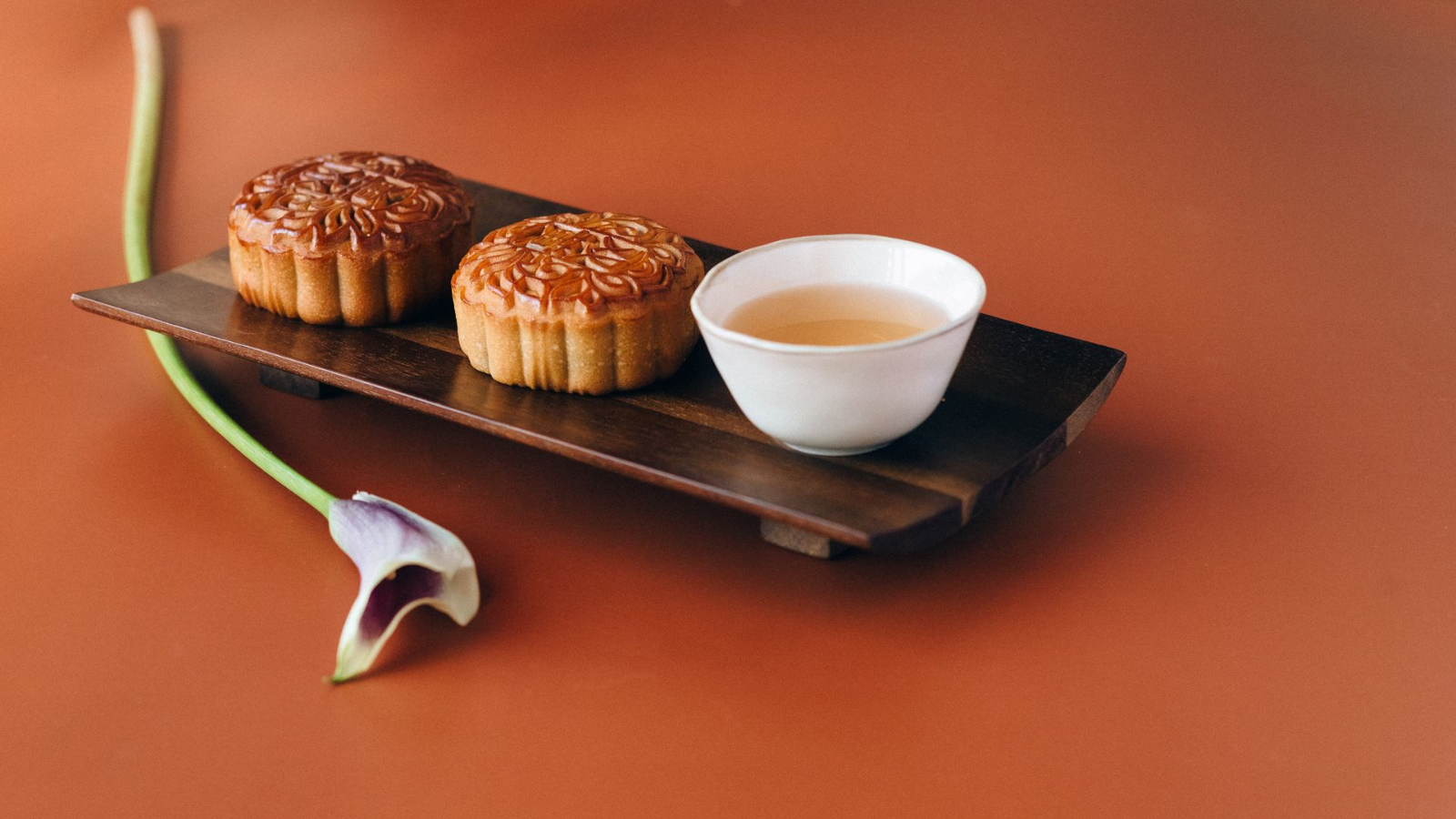 Mooncakes on wooden tray with white cup of tea and flower