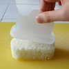 A hand holds a translucent white plastic rice mold over a rectangular block of white rice on a yellow cutting board, with a tiled kitchen background visible.