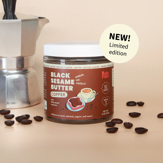 Jar of Black Sesame Butter Coffee surrounded by coffee bans and next to coffee pot on pinkish background
