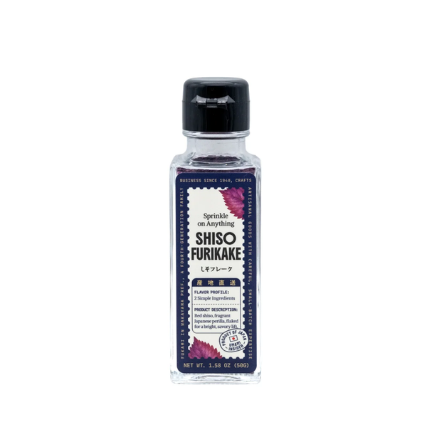 A bottle of Shiso Furikake seasoning by The Art of Seasoning, featuring a clear glass bottle with a black cap and a dark purple label decorated with pink shiso leaves.
