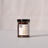 A small glass jar of XO Sauce, Medium Spicy, with a black lid and a white label, set against a clean, light gray background.