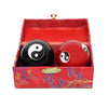 A pair of cloisonné metal therapy balls. One is red, the other black. Both having the yin yang symbol on them