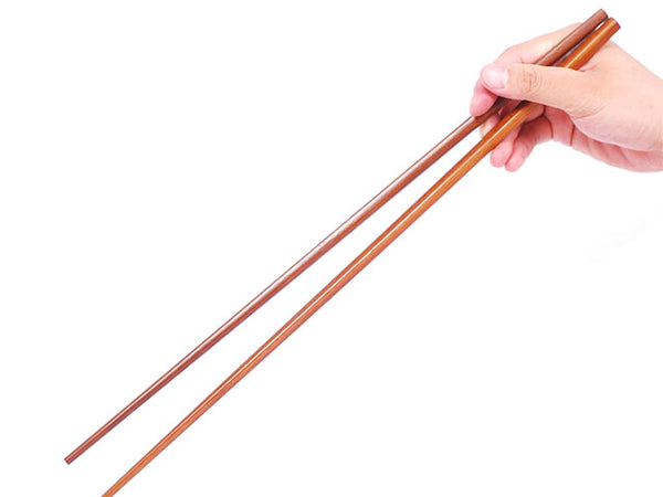 A pair of extra long wooden chopsticks being held by someone