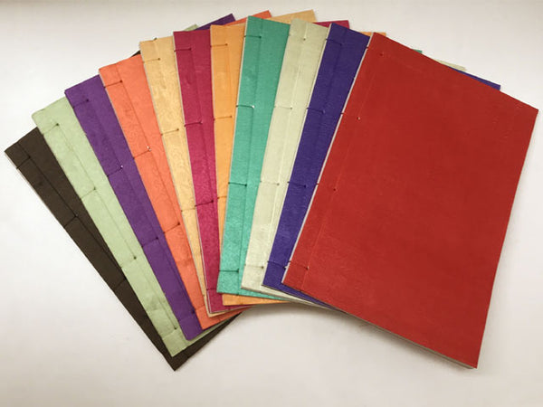 An array of silk covered bound journals. Their individual colors are: Brown, lime, purple, orange, yellow, red, magenta, green, yellow green, and blue